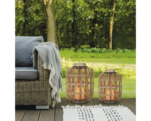 Gartenszene mit Rattansessel, Decke, Teppich und zwei Windlichtern aus Rattan mit LED-Kerzen.