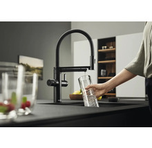 Schwarze Küchenarmatur mit schwenkbarem Auslauf und Person, die ein Glas mit Wasser befüllt