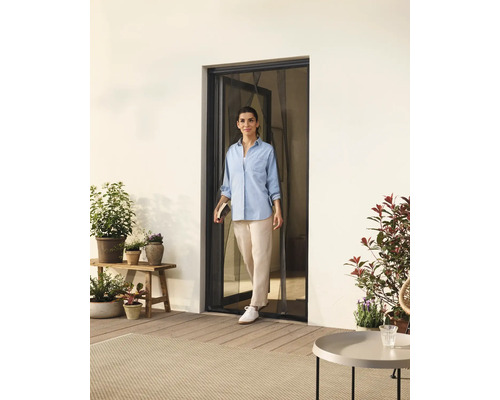 Femme franchissant une porte avec moustiquaire donnant sur une terrasse avec des plantes