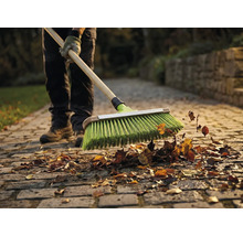 Une personne balaie des feuilles avec un balai sur une allée pavée.
