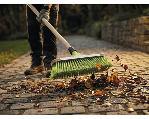 Une personne balaie des feuilles avec un balai sur une allée pavée.