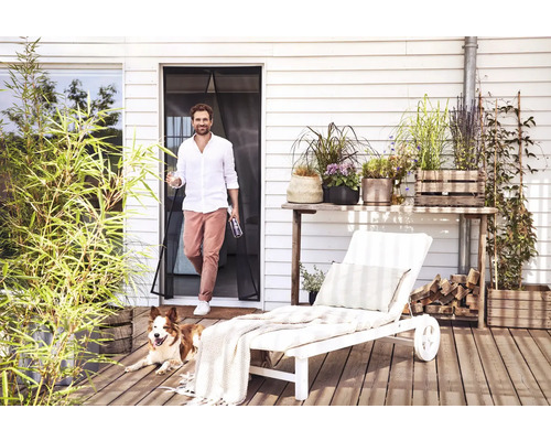 Extérieur avec homme, chien, porte moustiquaire, plantes et chaise longue sur une terrasse en bois