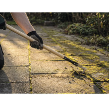 Une personne enlève de la mousse entre les pavés avec un nettoyeur de joints.