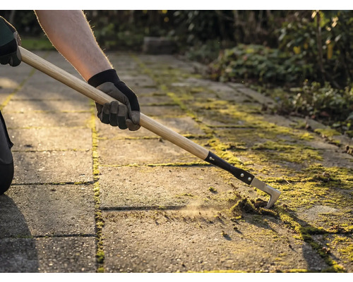 Une personne enlève de la mousse entre les pavés avec un nettoyeur de joints.