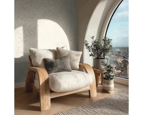 Helles Wohnzimmer mit einem hölzernen Sessel mit weichen Polstern, gemusterter Tapete und Zimmerpflanzen vor einem großen Bogenfenster.