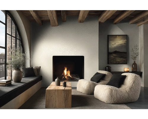 Gemütliches Wohnzimmer mit brennendem Kamin, zwei Teddy-Sesseln, Couchtisch aus Massivholz und Deckenbalken aus Holz im modernen Landhausstil.