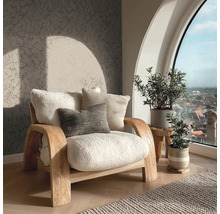 Heller Sessel mit Kissen neben Zimmerpflanzen und einem Fenster