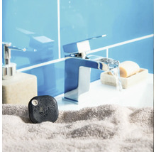 Détecteur de fuite d eau noir sur une serviette grise devant un robinet de lavabo dans une salle de bains lumineuse.