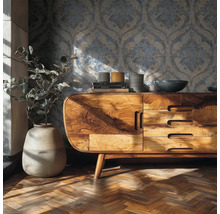 Wohnraum mit Ornament-Tapete, Sideboard aus Massivholz, Vase mit Pflanze und Fischgrätparkett.