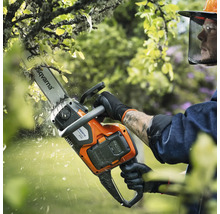 Une personne utilise une tronçonneuse à batterie Husqvarna pour élaguer un arbre.