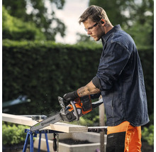 Un homme coupe du bois avec une tronçonneuse Husqvarna posée sur un établi.