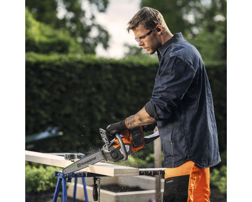 Un homme coupe du bois avec une tronçonneuse Husqvarna posée sur un établi.
