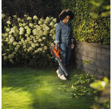 Une femme utilise un souffleur de feuilles à batterie dans le jardin pour enlever les feuilles.