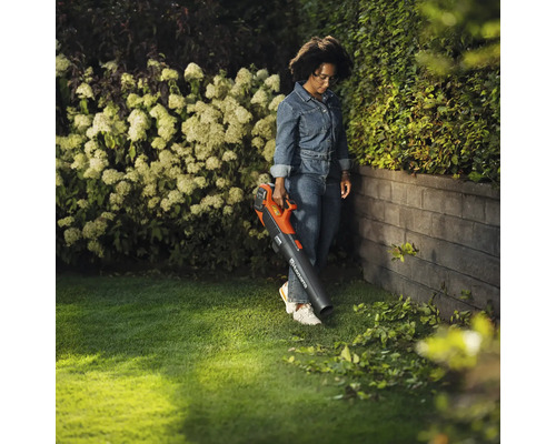 Une femme utilise un souffleur de feuilles à batterie dans le jardin pour enlever les feuilles.