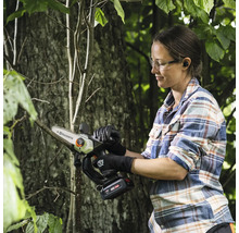 Une femme coupe une branche avec une scie à branches à batterie Husqvarna dans le jardin.