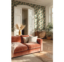 Wohnzimmer mit gemusterter Vliestapete, Samtsofa, Fischgrätparkett und Holzkommode in hellem Ambiente.