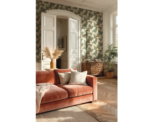 Wohnzimmer mit gemusterter Vliestapete, Samtsofa, Fischgrätparkett und Holzkommode in hellem Ambiente.