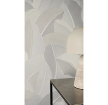 Vliestapete mit großflächigem, strukturiertem Blattmuster in neutralen Grautönen an einer Wand hinter einer modernen Tischlampe.
