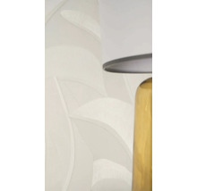 Vliestapete mit Blattmuster und Struktur in Hellbeige neben einer Tischlampe.