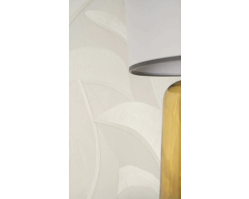 Vliestapete mit Blattmuster und Struktur in Hellbeige neben einer Tischlampe.