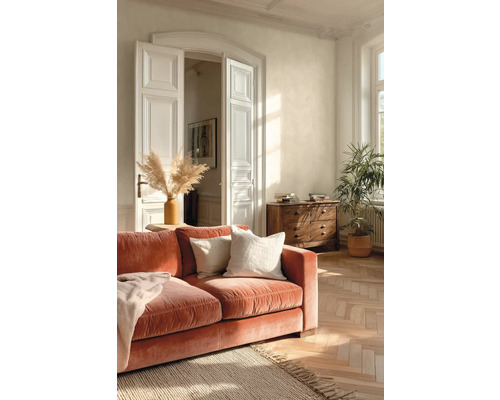 Heller Wohnraum mit Samtsofa in Terracotta, Fischgrät-Parkett aus Holz, weißer Flügeltür und einer Kommode aus Massivholz.