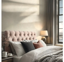 Helles Schlafzimmer mit gestepptem Kopfteil, strukturiertem Bettzeug, einer Tischleuchte und Sonnenlichtschatten auf der Wand.