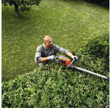 Une personne taille une haie avec un taille-haie dans un jardin.