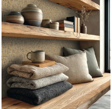 Étagère en bois rustique et mur avec papier peint texturé, vases, coussins et couvertures empilées dans un salon confortable.