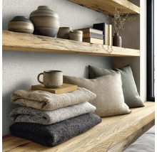 Strukturierte Wandbekleidung in einem hellen Raum mit Holzregalen, Keramik, gefalteten Decken und Kissen im modernen Naturstil.