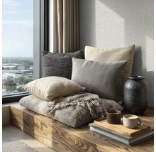Gemütliche Sitzecke auf einer Holzbank am Fenster mit strukturierten Kissen, einer gewebten Decke, einer Vase und Kaffeetassen auf einem Tablett.