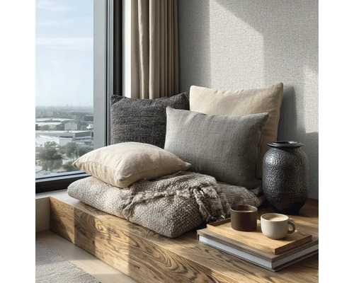 Gemütliche Sitzecke auf einer Holzbank am Fenster mit strukturierten Kissen, einer gewebten Decke, einer Vase und Kaffeetassen auf einem Tablett.