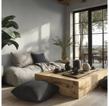 Modernes Wohnzimmer mit hellgrauer Wandfarbe, massivem Holztisch, Bodenkissen und großer Fensterfront zum Balkon.