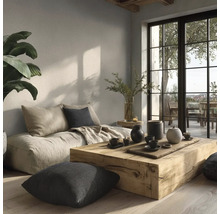Helles Wohnzimmer mit massivem Holztisch, bodentiefem Sofa, Kissen und großen Fenstern im minimalistischen Stil mit natürlicher Wandgestaltung.
