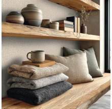 Wandgestaltung mit strukturierter Vliestapete in Leinenoptik, kombiniert mit massiven Holzregalen, Keramik und weichen Strickdecken.