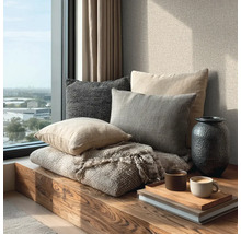 Gemütliche Sitzecke am Fenster mit Holzbank, verschiedenen Kissen, Wolldecke, Vase und Tablett mit Kaffeetassen auf Büchern.