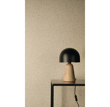 Papier peint intissé avec structure en lin et aspect tissé, au premier plan une lampe de table moderne avec abat-jour noir et pied en bois.