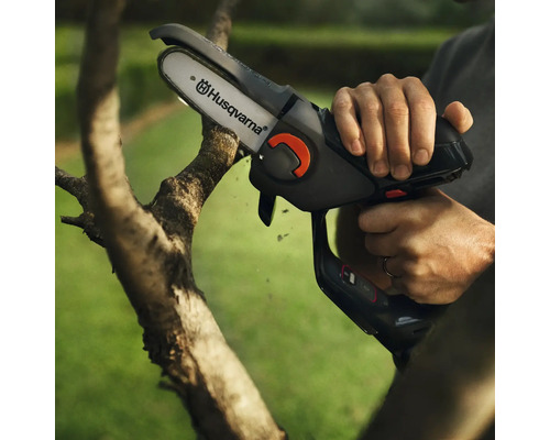 Une personne utilise une tronçonneuse à batterie Husqvarna pour couper une branche.