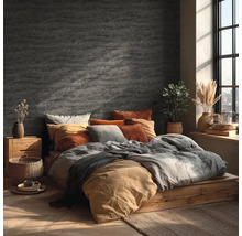 Chambre avec décoration murale aspect pierre, lit en bois, textiles aux tons terreux et lumière du jour vive par une fenêtre.
