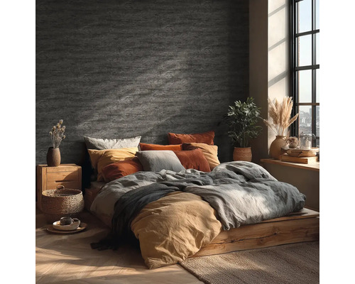 Chambre avec décoration murale aspect pierre, lit en bois, textiles aux tons terreux et lumière du jour vive par une fenêtre.