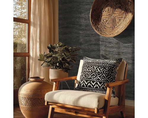 Papier peint gris foncé aspect pierre dans un salon rustique avec fauteuil en bois, vase en terre cuite et plante verte.