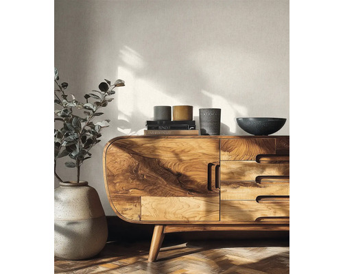 Helles Wohnzimmer mit einem modernen Sideboard aus Holz mit abgerundeten Ecken und markanter Maserung vor einer strukturierten Tapete.