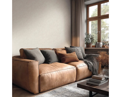 Wohnzimmer mit braunem Ledersofa, Dekokissen und strukturierter Wand neben einem Holzfenster. Helle und organisierte Atmosphäre.