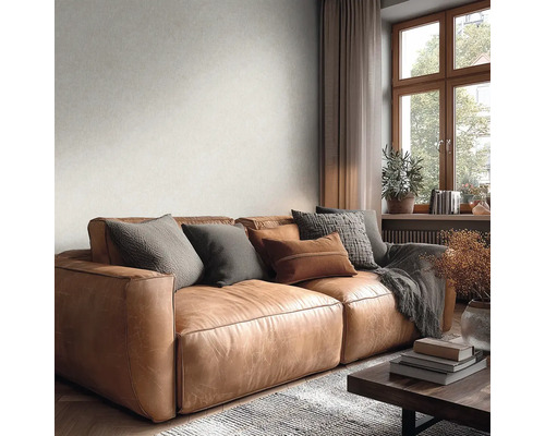 Helle, dezent strukturierte Tapete an der Wand hinter einem braunen Ledersofa in einem gemütlichen Wohnzimmer mit Fensterausblick.