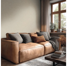 Gemütliches Wohnzimmer mit braunem Ledersofa, Kissen, beiger Strukturtapete und Holzfenster.
