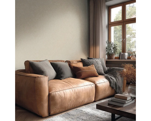 Gemütliches Wohnzimmer mit braunem Ledersofa, Kissen, beiger Strukturtapete und Holzfenster.