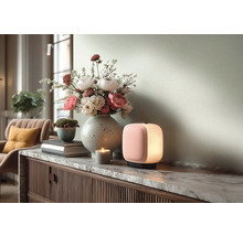 Moderne tragbare Tischleuchte mit rosa Front und weißem Licht auf einem Sideboard mit Marmorplatte neben einer Blumenvase und einer Kerze.