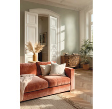 Helles Wohnzimmer mit hellgrüner Wand, rustfarbenem Samtsofa, Fischgrätparkett, Jute-Teppich und klassischer weißer Flügeltür.