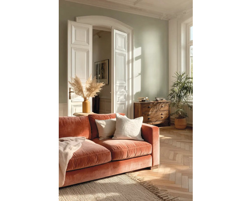 Helles Wohnzimmer mit hellgrüner Wand, rustfarbenem Samtsofa, Fischgrätparkett, Jute-Teppich und klassischer weißer Flügeltür.