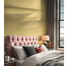 Helles Schlafzimmer mit gelber Wand, rosa gepolstertem Kopfteil, grauer Bettwäsche und einer Tischlampe neben einem großen Fenster.