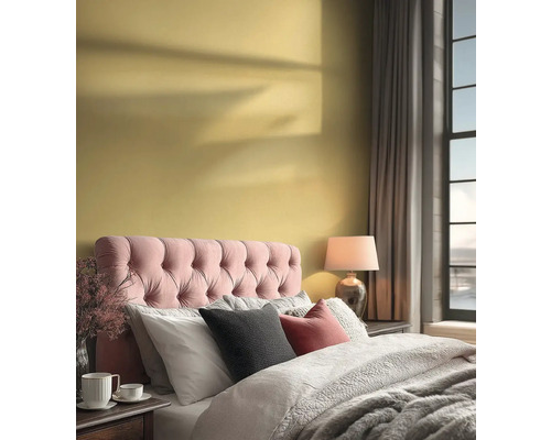 Helles Schlafzimmer mit gelber Wand, rosa gepolstertem Kopfteil, grauer Bettwäsche und einer Tischlampe neben einem großen Fenster.